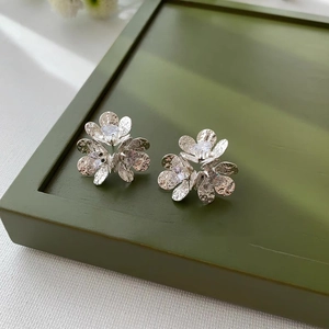 Macro detail of silver flower stud earrings with sparkling zircons and hammered texture
