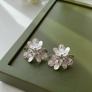 Close-up of elegant flower stud earrings with zircon centers on a dark green tray