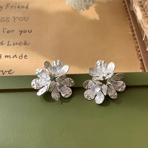 Detailed view of silver flower earrings with zircon centers on a textured metal surface