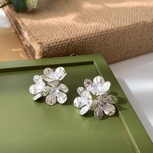 Detailed view of silver flower stud earrings with hammered petals and clear zircons