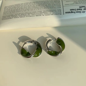 Detail of silver twisted hoop earrings with green resin inlays on a white background
