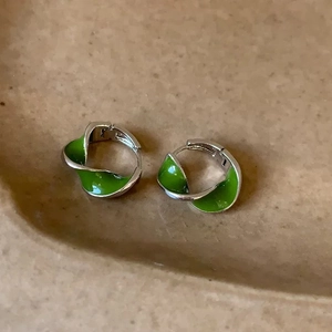 Macro shot of silver twisted hoop earrings with green enamel on a ceramic tray