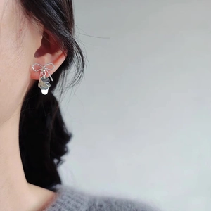 Elegant silver bow earrings with polished tassel discs worn on model against gray background