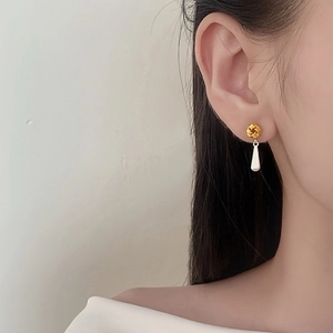 Elegant gold twisted knot earrings with white teardrop pendant on a female model
