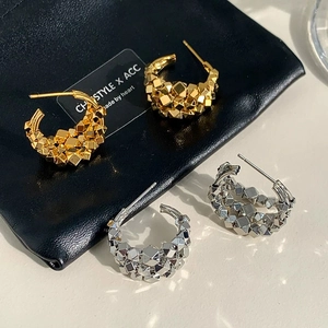 Macro detail of gold and silver C-shaped earrings with irregular geometric texture