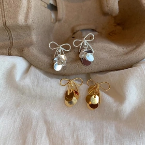 Detail of bow-knot dangle earrings in gold and silver finish on a rustic tray