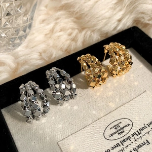 Macro detail of geometric C-shaped stud earrings with punk style metallic pyramid studs