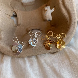 Polished gold and silver bow stud earrings with round disk fringe on natural background