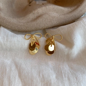 Detailed shot of gold bow earrings with metal sequins on a minimalist fabric background