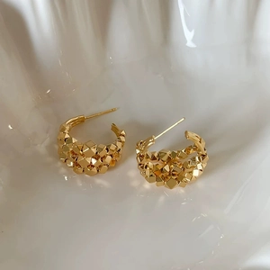 Detail of gold C-shaped earrings with geometric pyramid texture in white ceramic bowl
