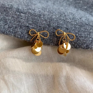 Detail of gold bow earrings with dangling sequins on textured knit background