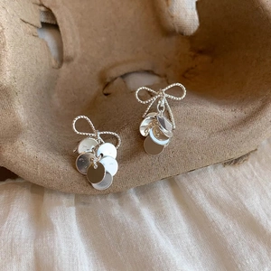 Detail of silver bow tassel earrings with polished metallic disks in elegant light