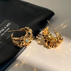 Macro detail of gold-plated geometric C-shaped hoop earrings with faceted texture
