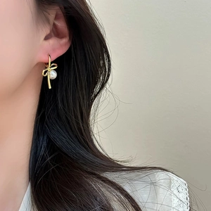 Elegant gold bow earrings with white pearls shown on model in a minimalist setting