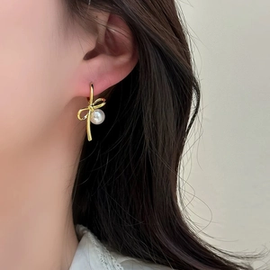 Detail of elegant gold bow earrings with pearl pendant worn by model for perspective