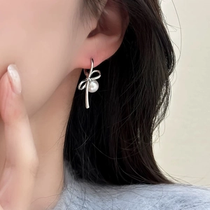 Close-up of elegant silver bow stud earrings with a white pearl on a female ear