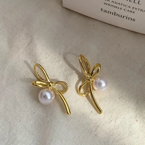 Detail shot of elegant gold bow stud earrings with white pearls on a soft linen surface