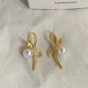 Detail view of French-style gold bow earrings with elegant white pearls on beige fabric