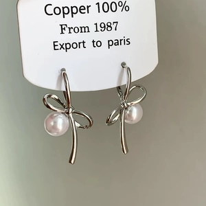 Detailed shot of silver bow pearl earrings on a white display card featuring 100% copper base