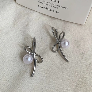 Detail of silver bow stud earrings with white pearls on a minimalist linen texture background