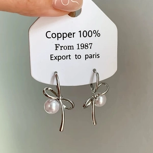 Detail of silver bow earrings with white pearls on a display card for women