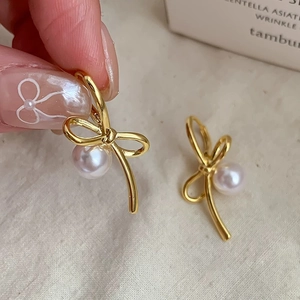 Elegant gold bow earrings with white pearls shown in hand against a soft fabric background