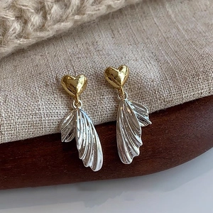 Detail view of heart-shaped gold studs with silver textured wing pendants on linen
