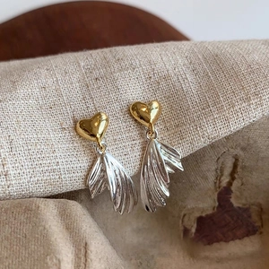 Macro shot of gold heart earrings with silver textured wing pendants on beige linen