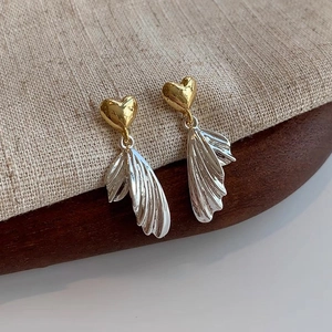 Detail of elegant gold heart and silver wing tassel earrings on a rustic base