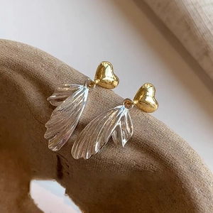 Detailed close-up of heart wing tassel earrings on a textured brown ceramic edge