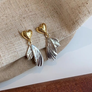 Detail of gold heart studs with silver textured wing tassels on a rustic burlap base