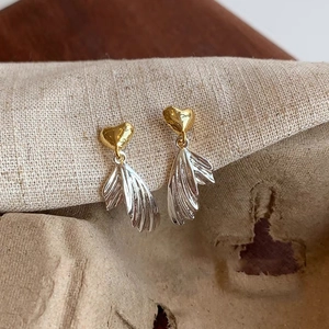 Close-up of elegant gold heart and silver textured fan fringe earrings on fabric