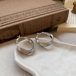 Detailed close-up of layered silver hoop earrings on white ceramic tray