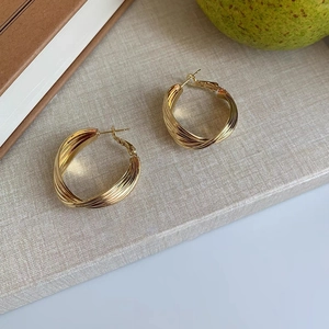 Detailed close-up of gold-plated spiral twisted hoop earrings on a soft texture background