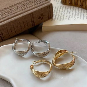Macro shot of twisted gold and silver C-shaped hoop earrings on a ceramic tray