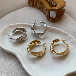 Close-up of twisted multi-layer hoop earrings in gold and silver finish on a ceramic plate