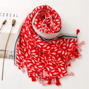 Detail of red leaf print scarf with tassels beside a lifestyle magazine on white surface