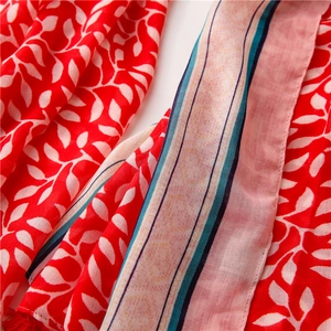 Close-up of red leaf print scarf featuring delicate tassels and striped edge detailing
