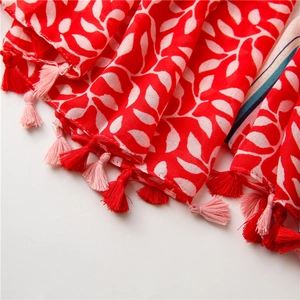 Close-up of red and white leaf print linen scarf featuring decorative tassel fringe details