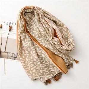 Detail of soft earth-tone scarf with leaf prints and decorative fringe tassels