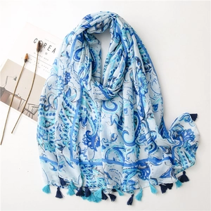 Detail of light blue linen scarf with paisley prints and thick blue tassels on white base