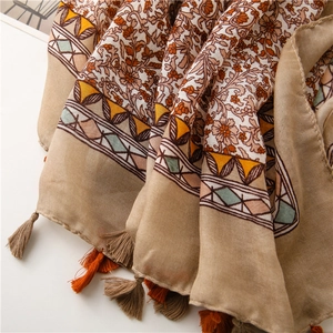 Detailed view of bohemian floral print scarf with orange tassels and cotton linen texture