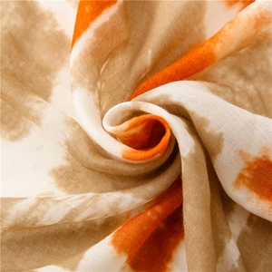 Close-up of tie-dye scarf fabric showing soft orange and brown spiral texture
