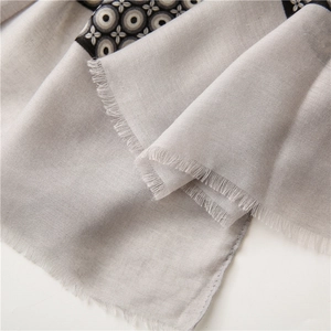 Detail of light grey cotton linen scarf featuring geometric circle patterns and long tassels