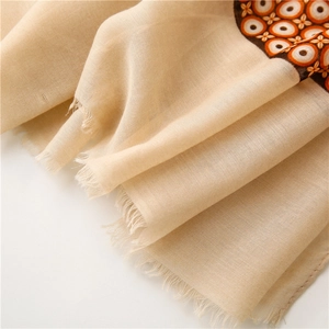 Close-up of beige linen scarf featuring orange geometric patterns and delicate fringe