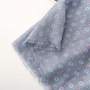 Detail of soft gray scarf featuring blue geometric square patterns and delicate fringe