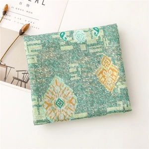 Detail of green scarf with geometric paisley pattern next to dried flowers and magazine