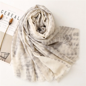 Close-up of lightweight grey and white tie-dye scarf with frayed tassel edges on magazine