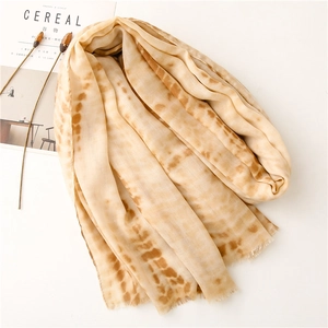 Detail shot of beige cotton linen scarf with irregular dark tie-dye pattern and fringe edges