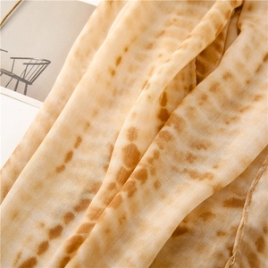 Detailed macro view of soft beige cotton linen texture scarf with orange tie-dye pattern